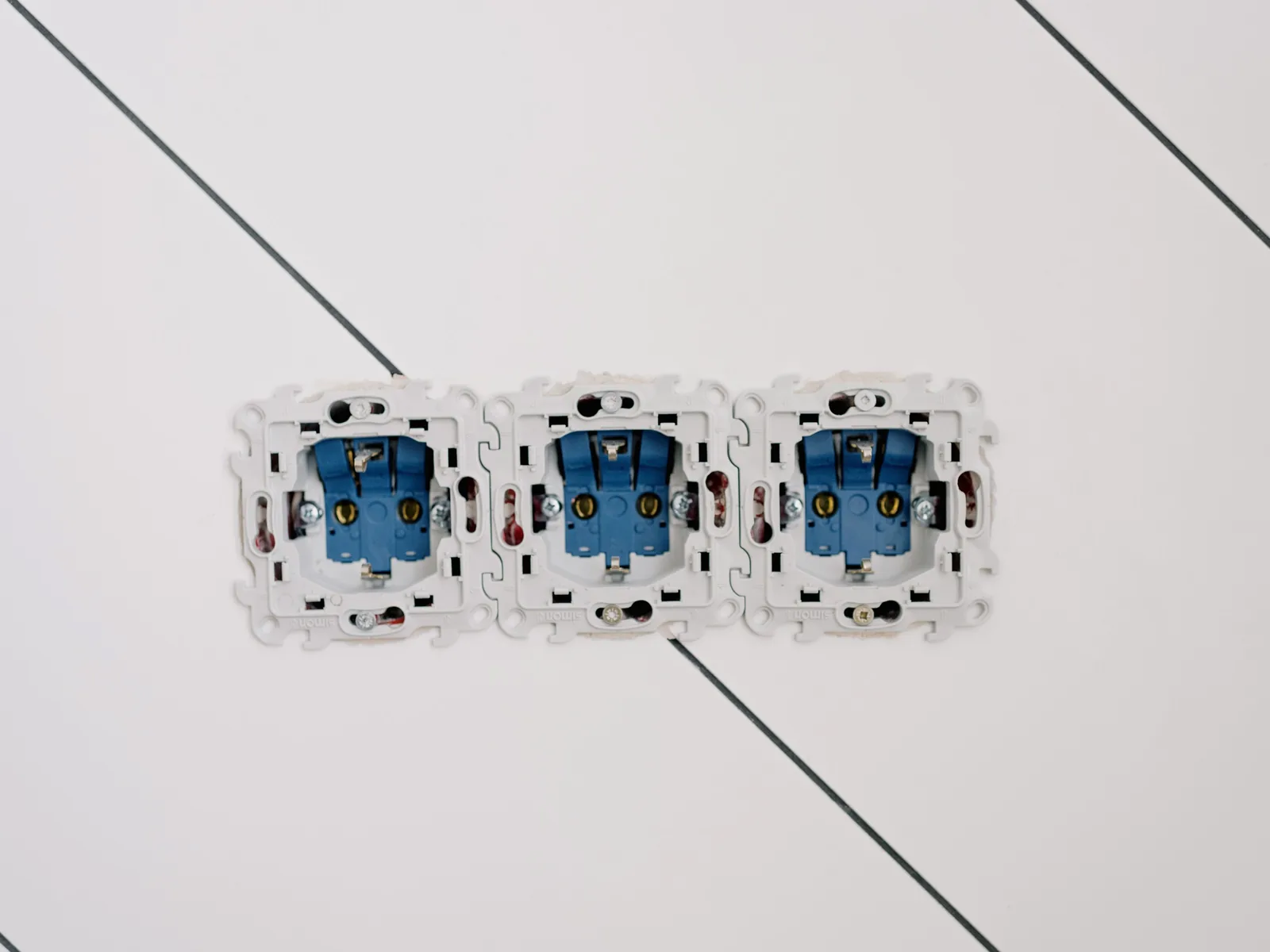 Tres mecanismos de enchufe con sus bornes y garras a la vista, aún sin embellecedor