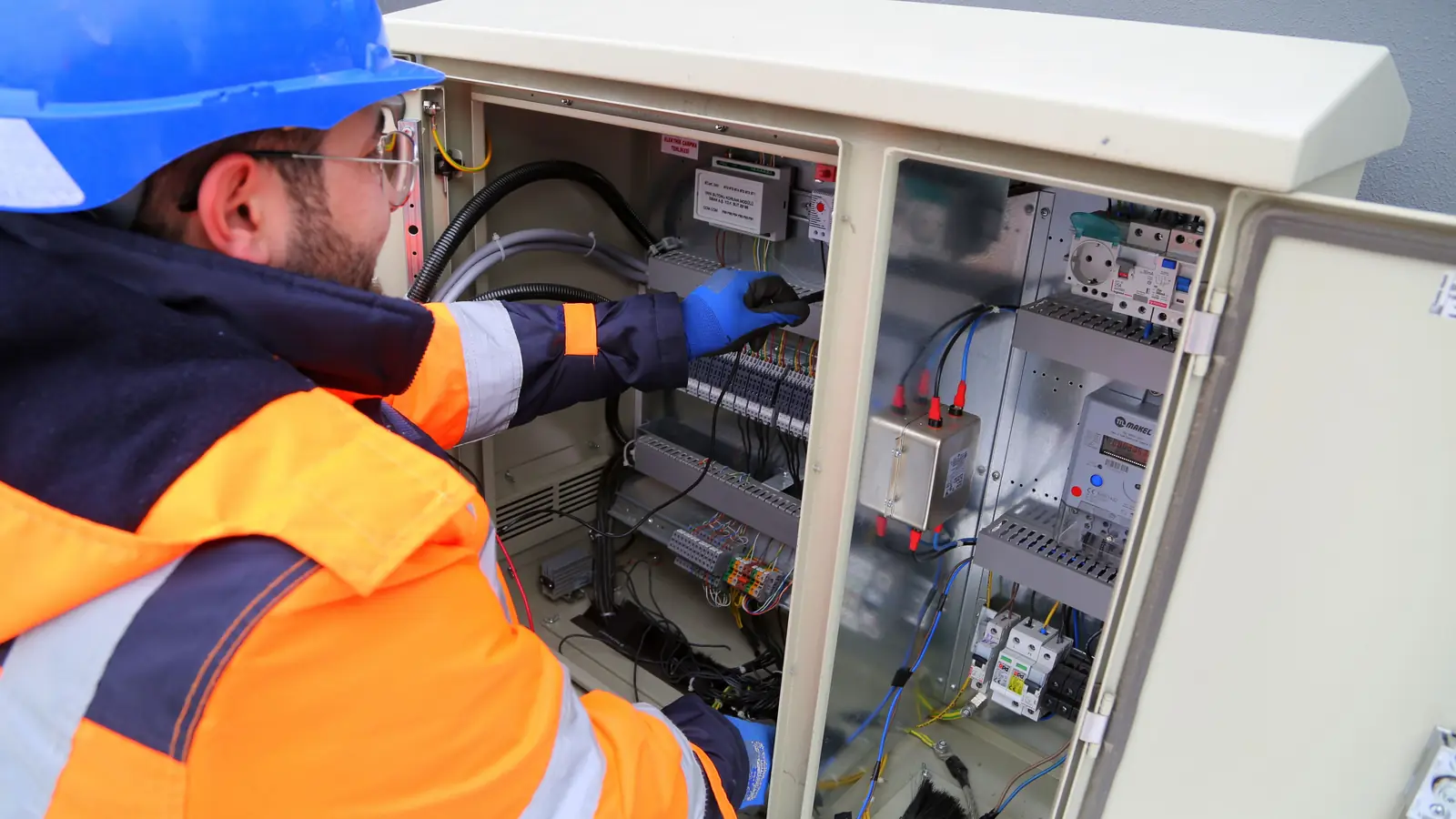 Electricista con equipo de protección trabajando en un armario eléctrico abierto
