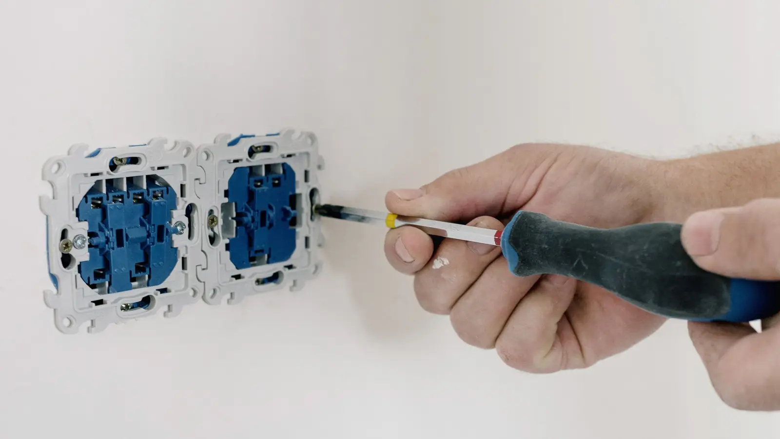 Mano con destornillador apretando dos mecanismos eléctricos sin embellecedor en una pared